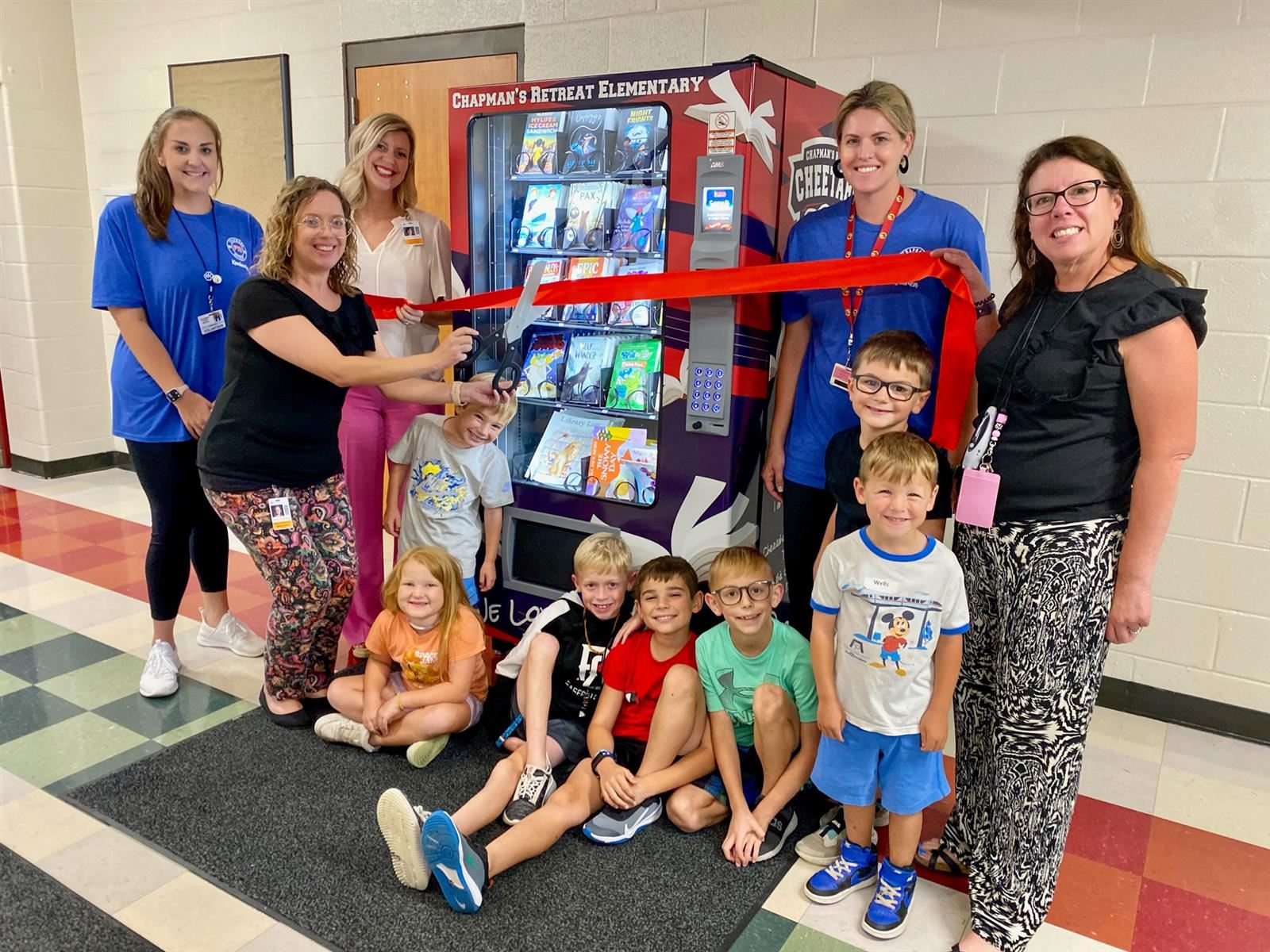 parents, principal and students cutting a ribbon on a vending machine